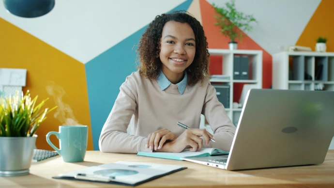 Young woman smiling at desk with laptop and coffee.